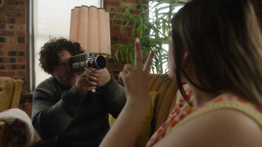 Man capturing a joyful woman on a video camera while both are seated on the living room couch