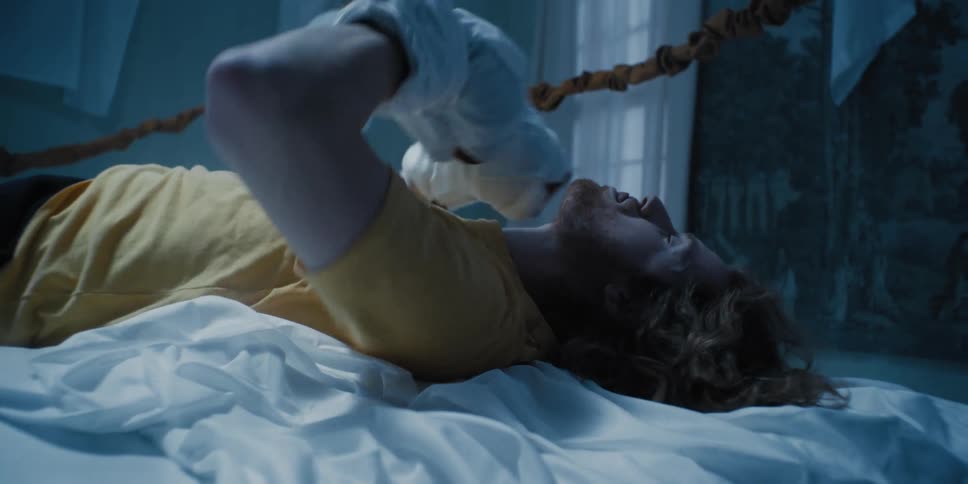 Man lying down on a boxing ring made of bed sheets wearing bed sheets around his fists punches one against the other and stands up