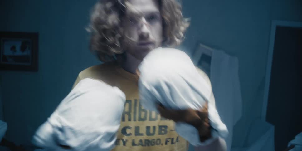 A man wearing white sheet gloves punching forward toward something in a disheveled room