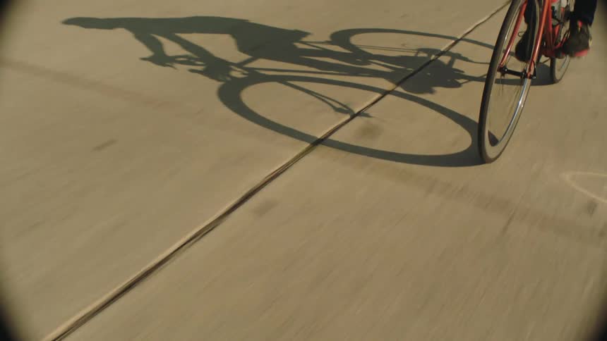 Black man riding a bike on the road passing through parked cars on the side