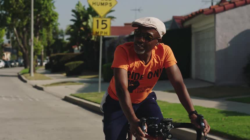 A man looks around at his surroundings as he rides a bicycle through a residential neighborhood during the day