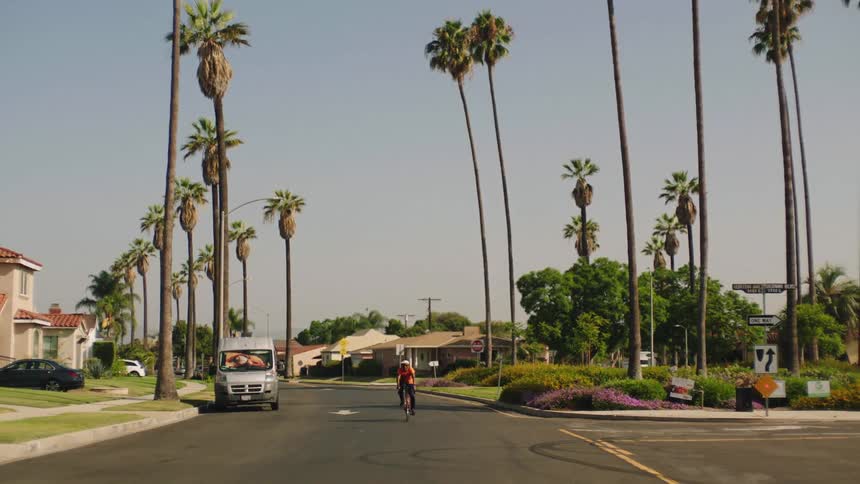 A cyclist rides a bicycle down a road through a residential neighborhood during the day