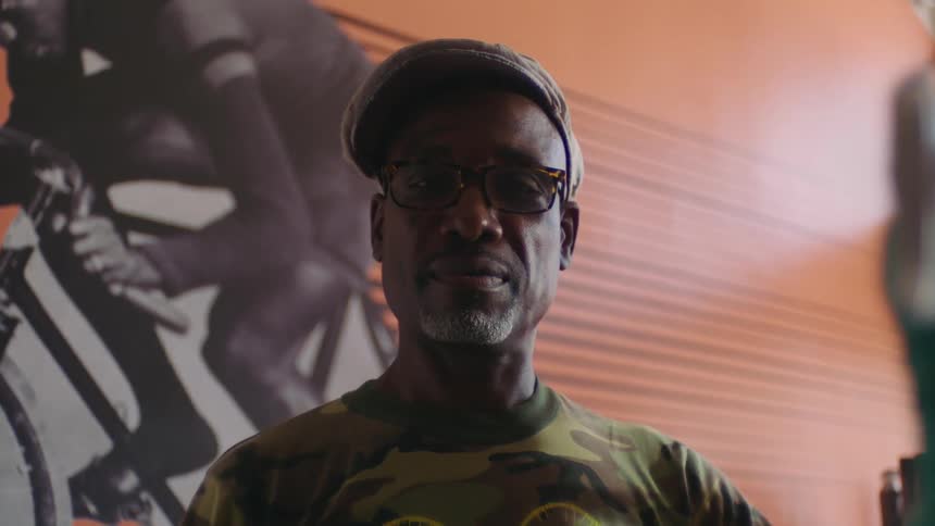 A man looks into the camera while posing with a bicycle indoors during the day