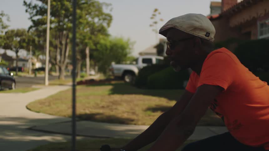 A man looks around at his surroundings while riding a bicycle through a residential neighborhood during the day