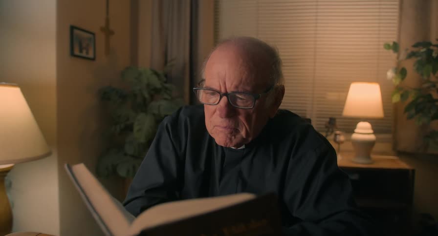 An old man reads through a book by lamp light