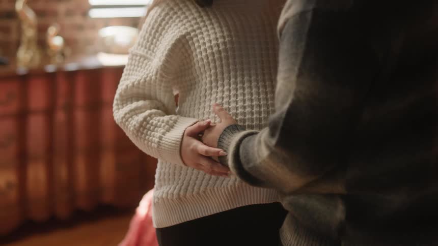 Close up of a man rubbing a womans pregnant belly over her white sweater as they sway back and forth