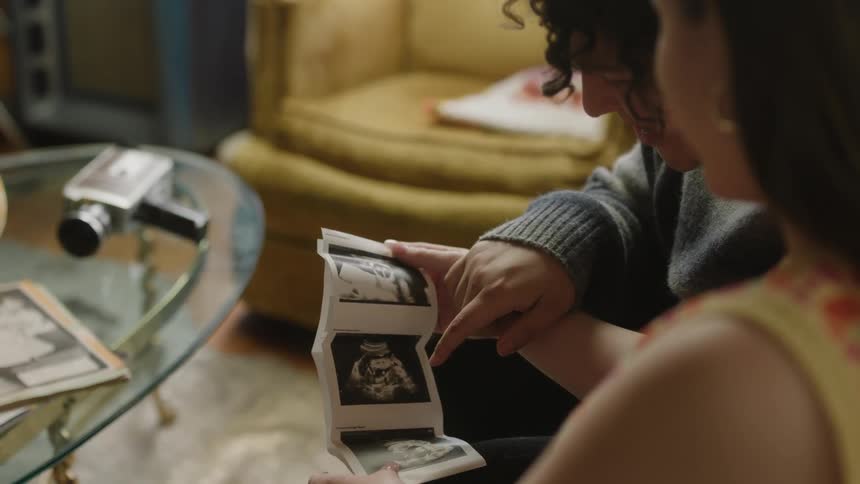 A close up of a young man and woman looking at photographs together in their living room