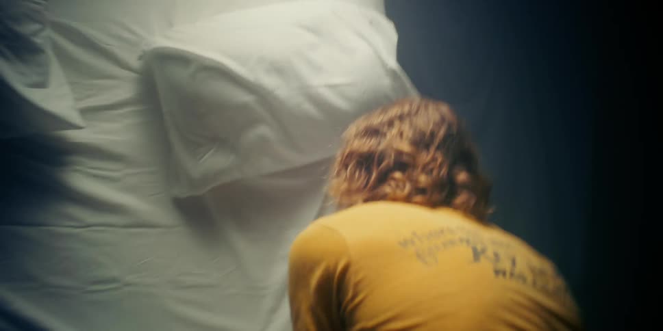 A man sleeping in bed jumps up and looks frightened and looks down at the bed