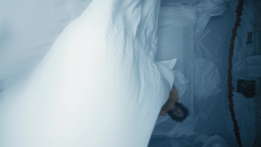 Aerial view of a man lying in bed with a sheet floating tied to the ceiling