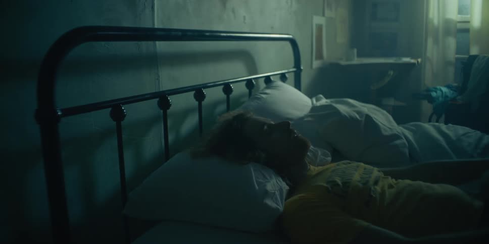 A man lies down in a bed and adjusts the pillow beneath his head before pulling up a bed sheet to cover his chest during the day