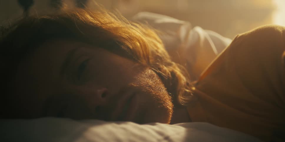 A man sleeping in bed opens his eyes as someone beside him moves