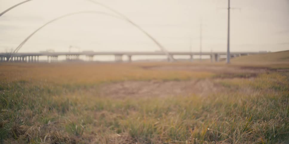A still shot of a grassy field before a distant bridge with many cars driving past