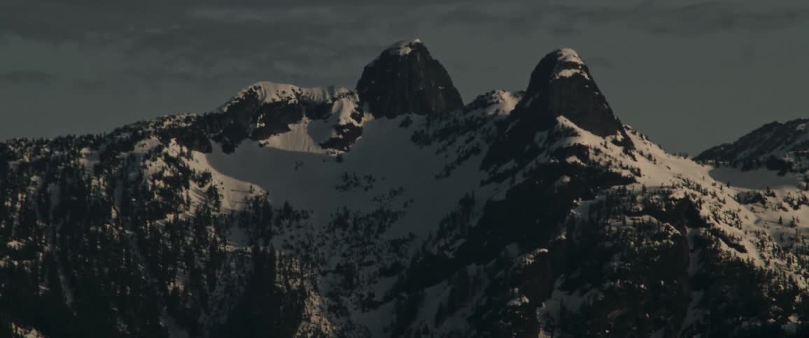 A mountain ridge covered in snow and forest in the evening