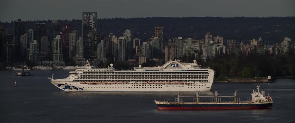 A cruise ship passes by a big city on the waterfront and a plane flies by
