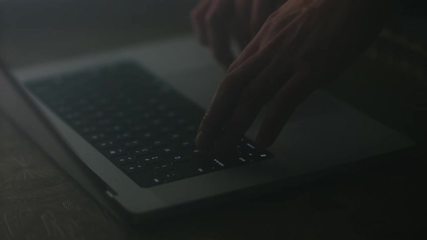 A pair of hands types slowly on a laptop computer