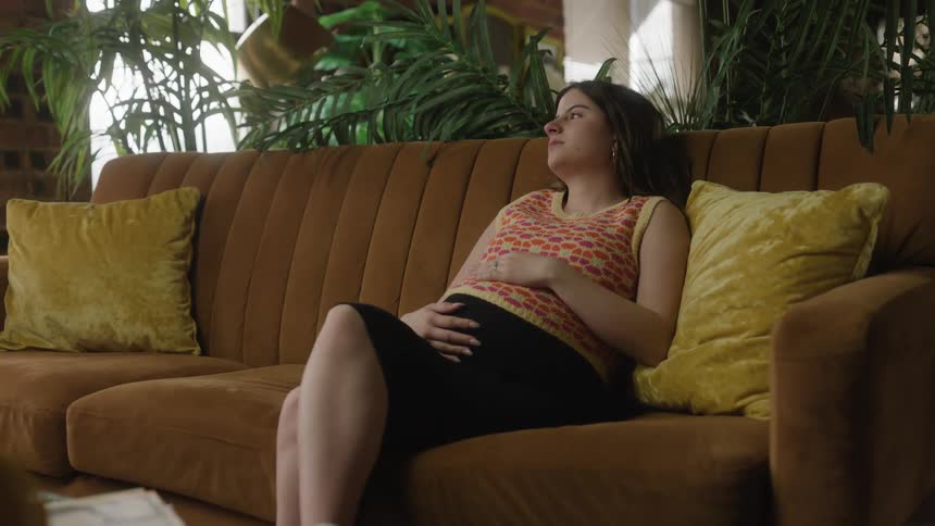 A pregnant woman is sitting on the couch