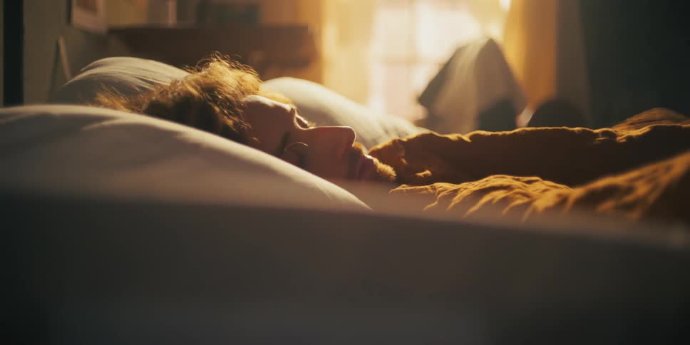 A close up of a man laying in bed under the blankets as the sun shines through his window