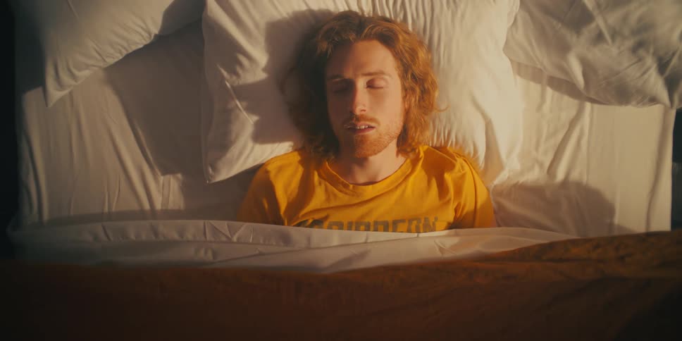 Man lying in bed with a blanket falling over his body