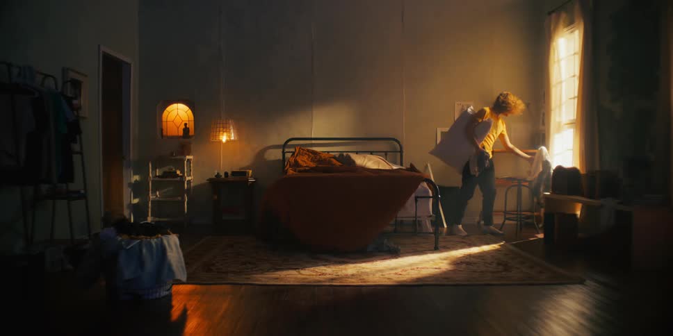 A curly haired man tidies up his bedroom