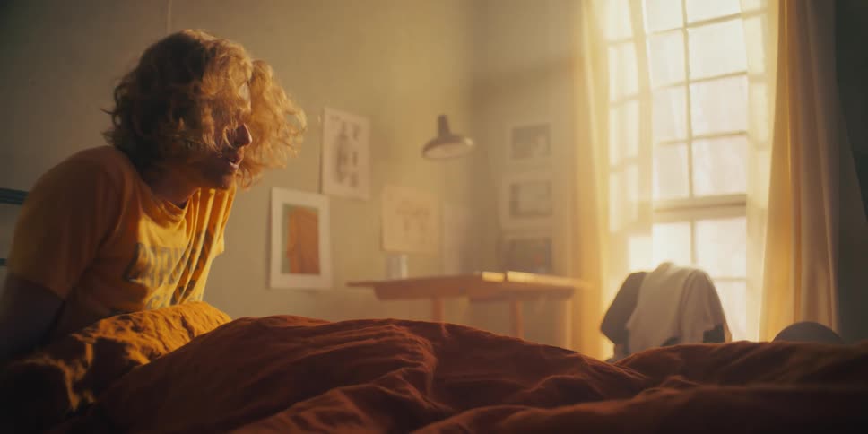 A man sits in his bed as he wakes up then angrily pulls the blanket and sheet off him