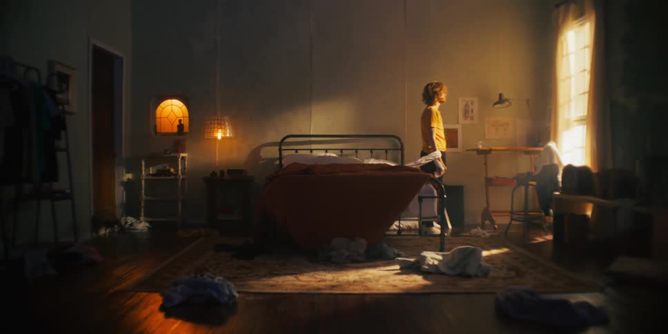 Man getting out of bed in a messy room with clothes thrown on the floor