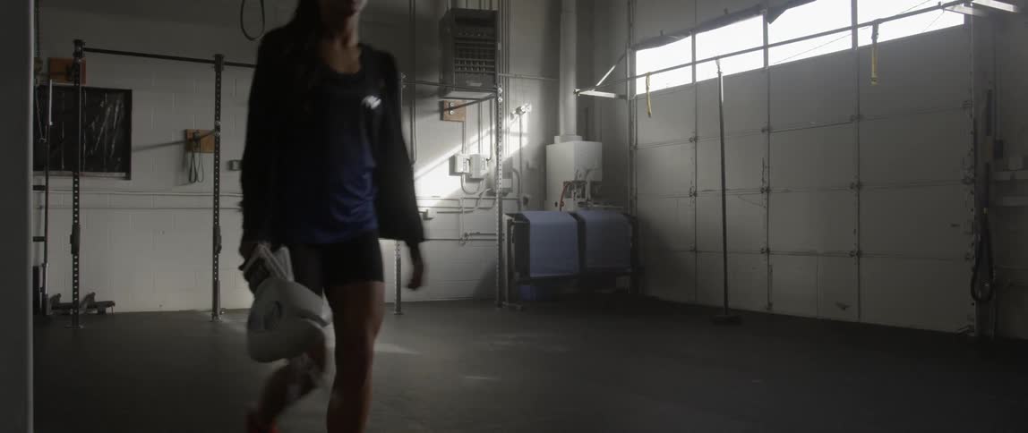 A woman walks across a room carrying boxing gloves