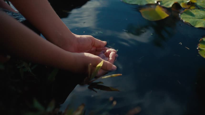 A pair of hands picking water from a lake and bringing it up to drink