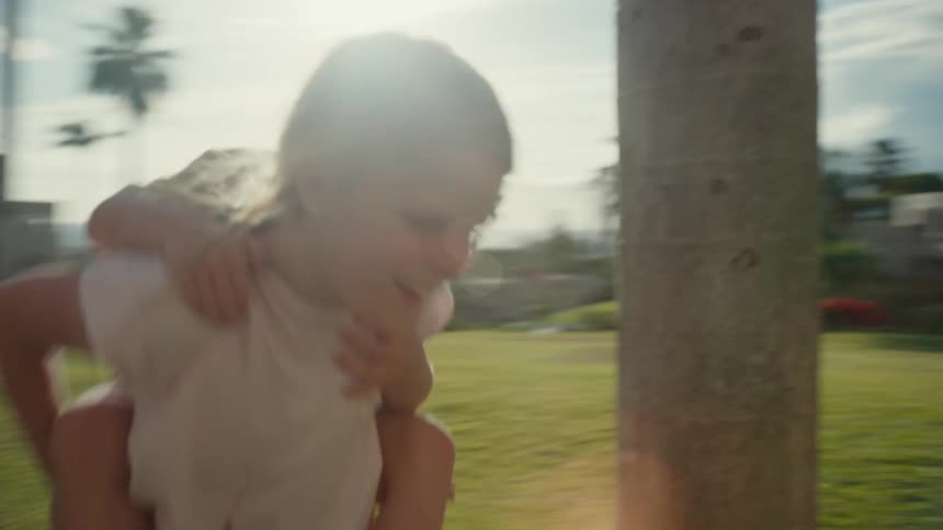 A little girl runs in circles as she carries her younger brother on her back in their yard