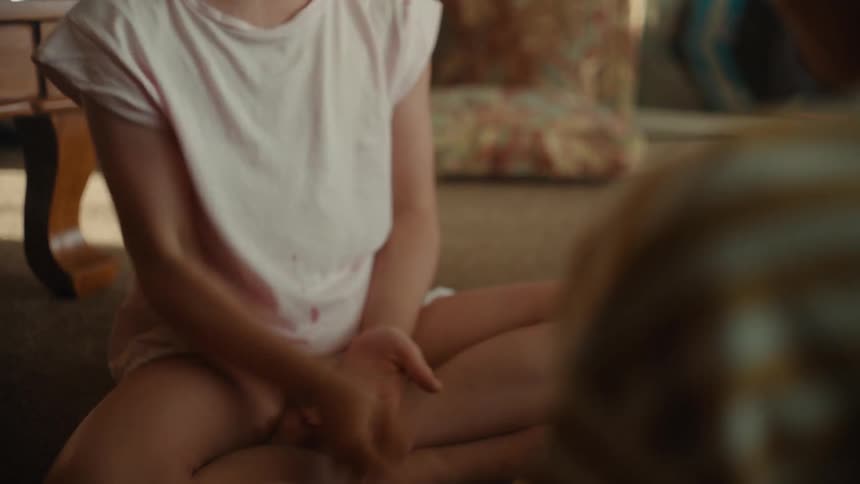 A girl plays paper rock scissors with a boy while they sit together on the floor indoors during the day