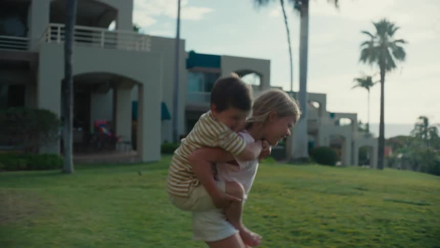 A girl playfully runs through a field while carrying a boy on her back
