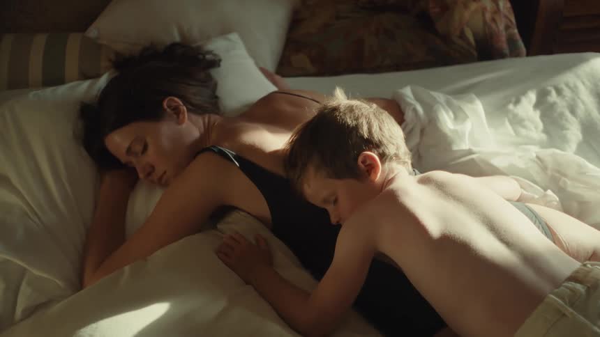 A young boy sleeping on his mothers back as sunlight falls on them