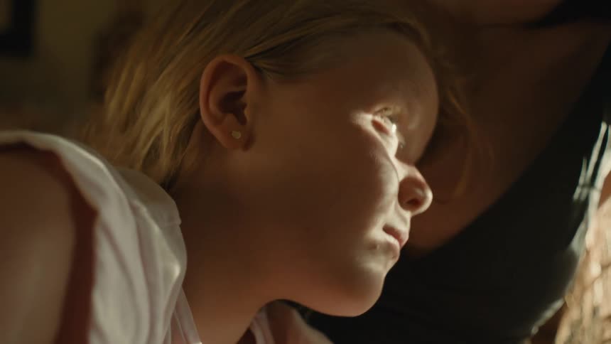 Mother caresses blonde hair of daughter as they sit in shade outside