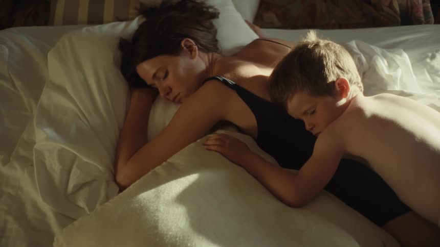 Boy napping on the back of his mother who is sleeping on the bed