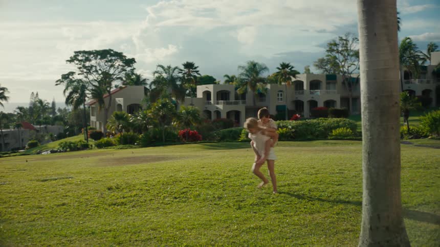 A young girl spinning around in grass with her younger brother on her back