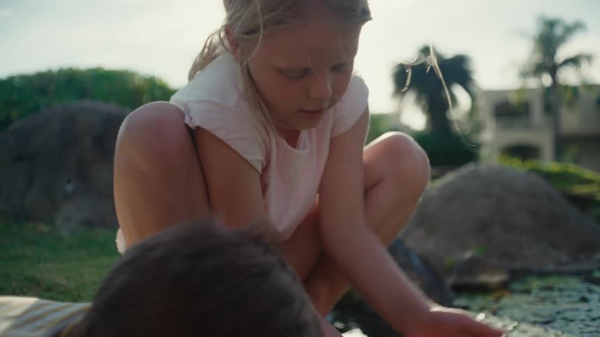 Boy and girl crouch near pond examining the water