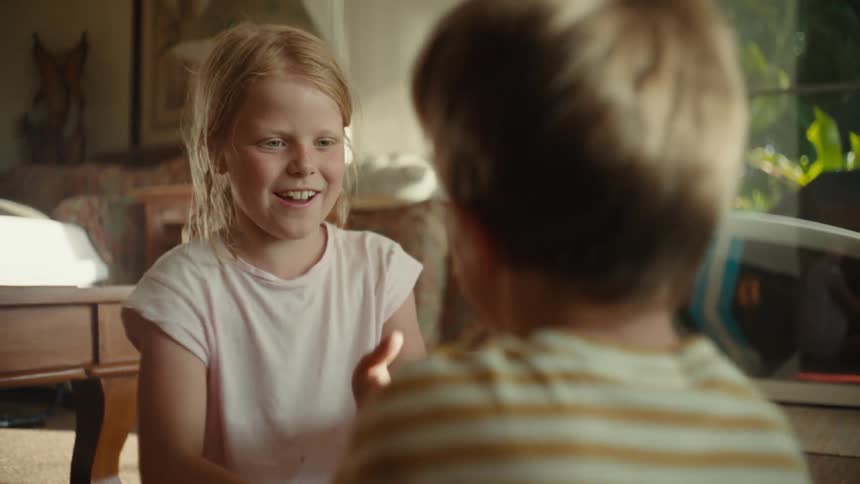 Young brother and sister sitting on the living room floor as they play rock paper scissors