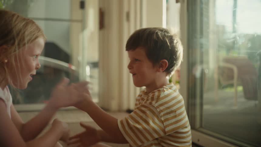 A brother and sister play hand games on the floor of their home