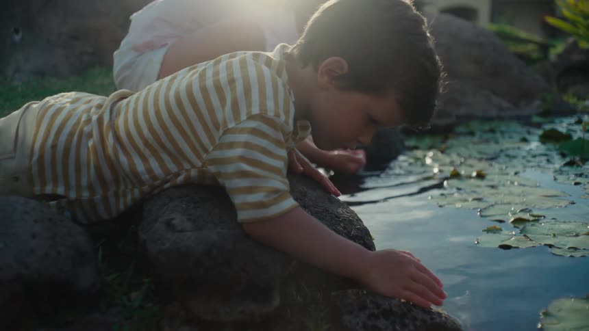 Small boy and girl playing with water next to a pond