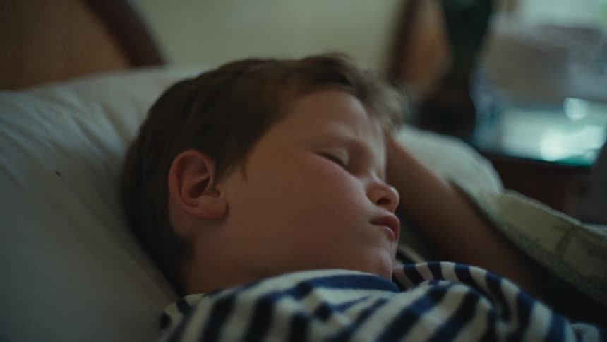 A close up of a boy sleeping in a bed opening his eyes and then closing them again