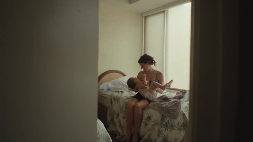 Mother holding her baby and joyfully playing with him on the bed