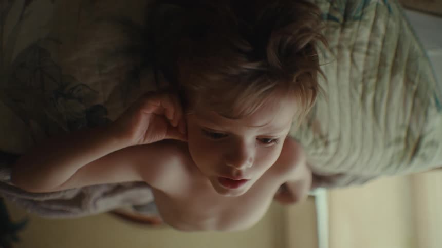 Boy leans with his head off the bed and stares