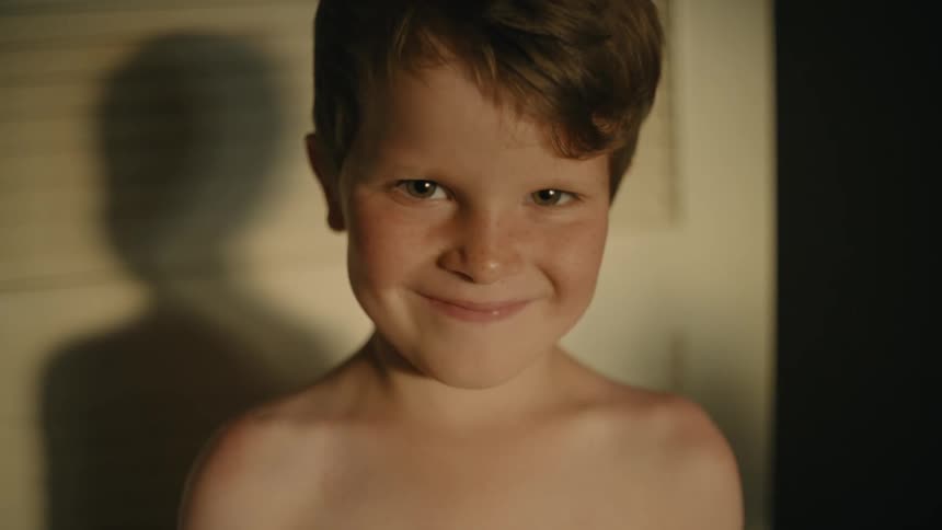 A little boy is looking ahead with a serious look on his face and then he smiles and laughs