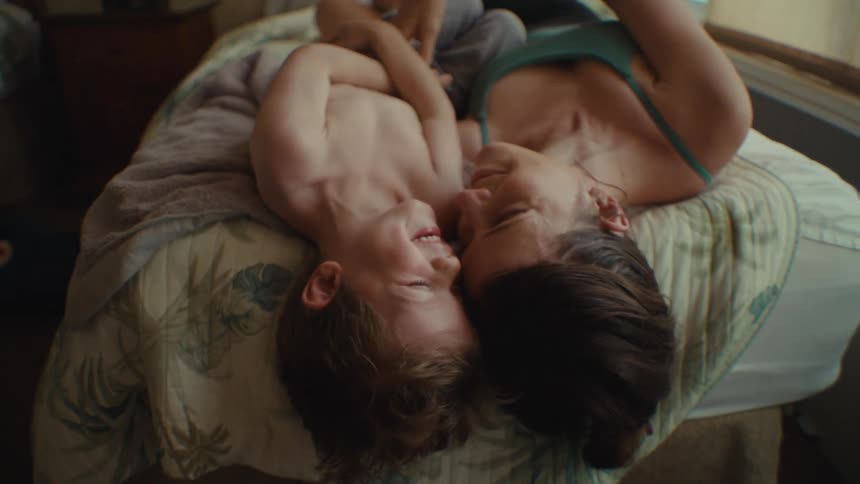 A mother and son laugh in bed