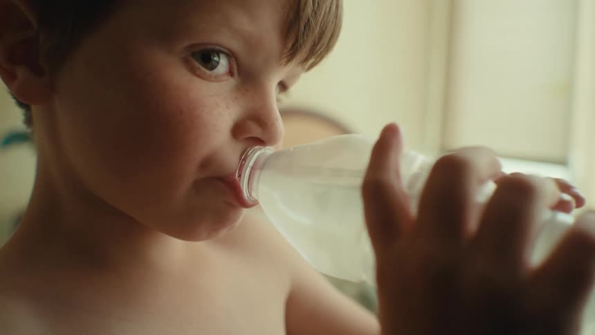 A young boy drinking from a water bottle in the bedroom