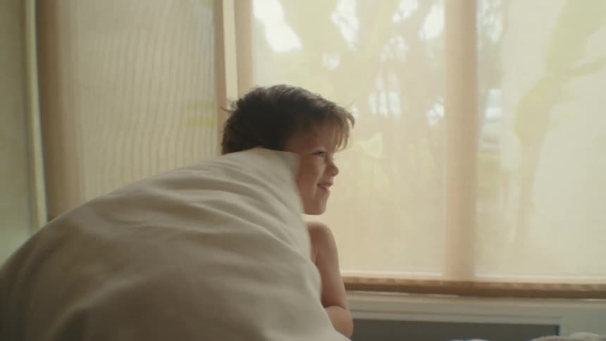 A pair of young boys have a pillow fight in a bedroom during the day