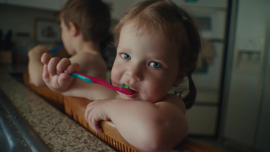 A boy and girl brush their teeth at the kitchen sink