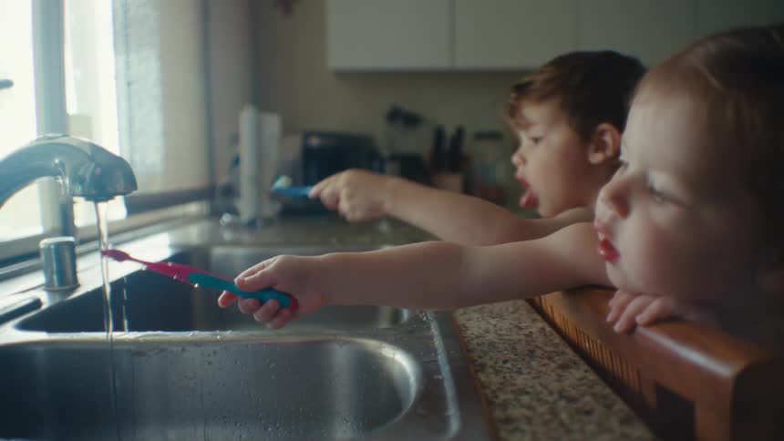 A boy and girl leaning over to get water on their tooth brushes