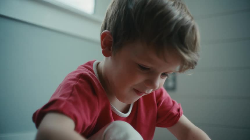 Boy wearing a red shirt sitting on the floor smiling and playing