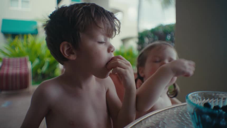 Children eat berries from a glass bowl sitting at a table outdoors