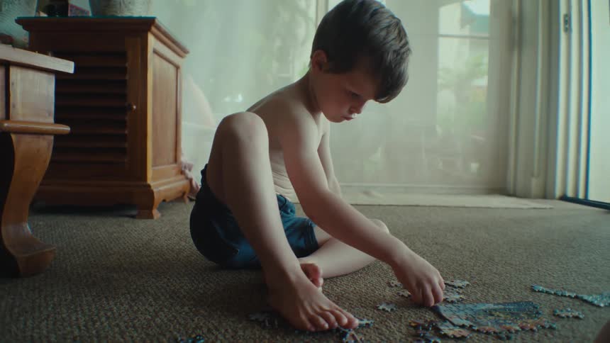 A young boy sits on the floor and carefully pieces together a puzzle
